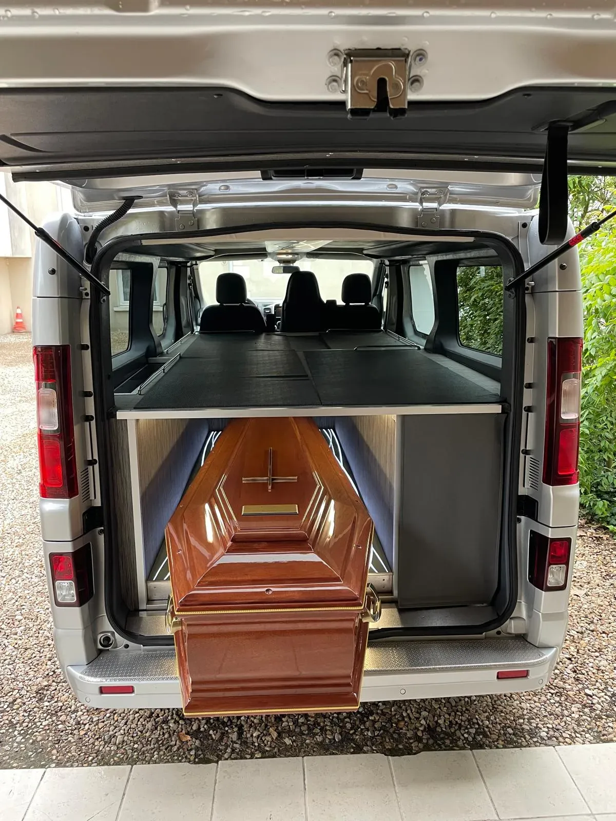 Cercueil en bois posé dans le coffre ouvert d'un véhicule funéraire adapté.