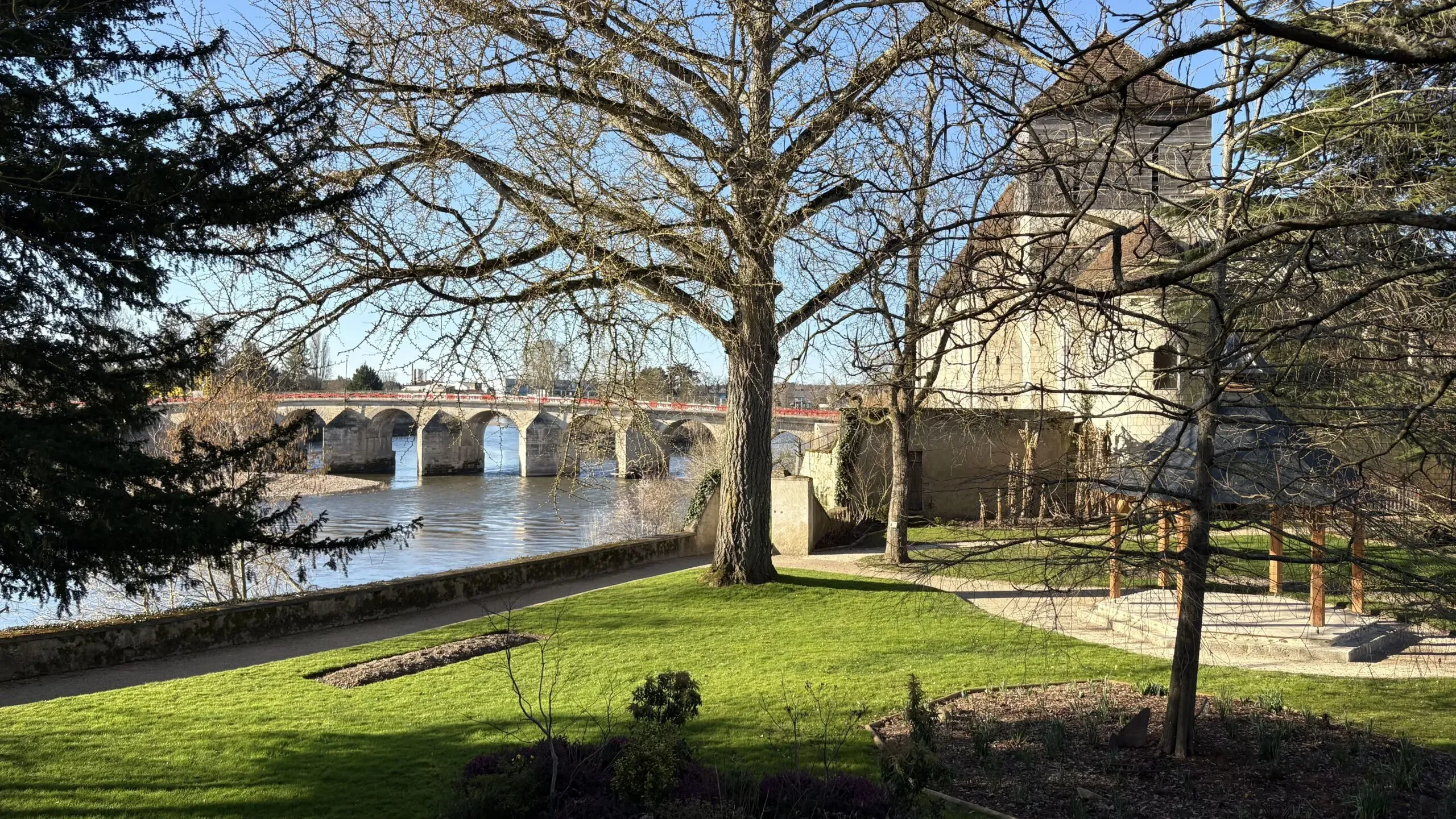 Parc verdoyant avec arbres et pont en pierre au bord de la rivière.