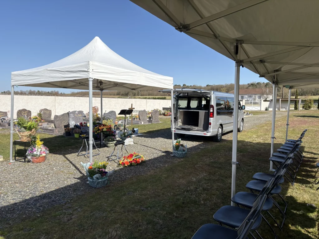 Espace de cérémonie funéraire en extérieur sous chapiteau avec fleurs et sièges.