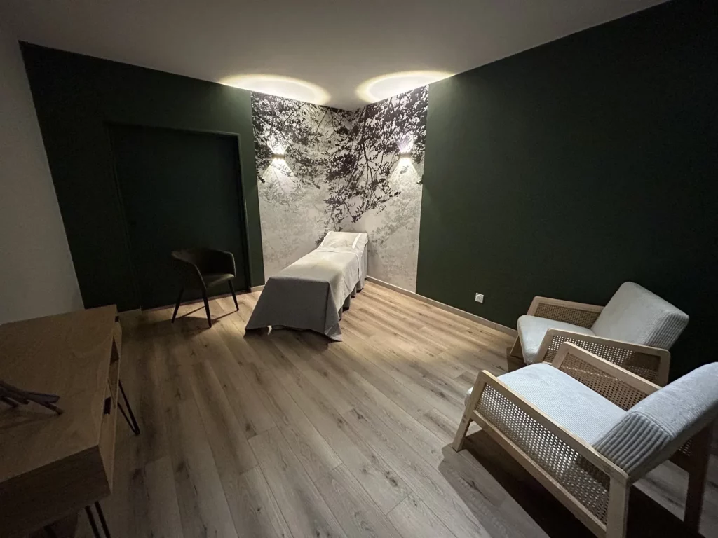 Salon funéraire paisible aux murs vert foncé avec lit de repos et fauteuils.