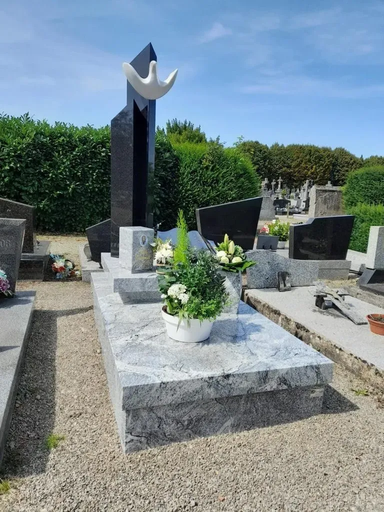 Monument funéraire moderne en granit gris et noir orné de fleurs et d'une colombe.